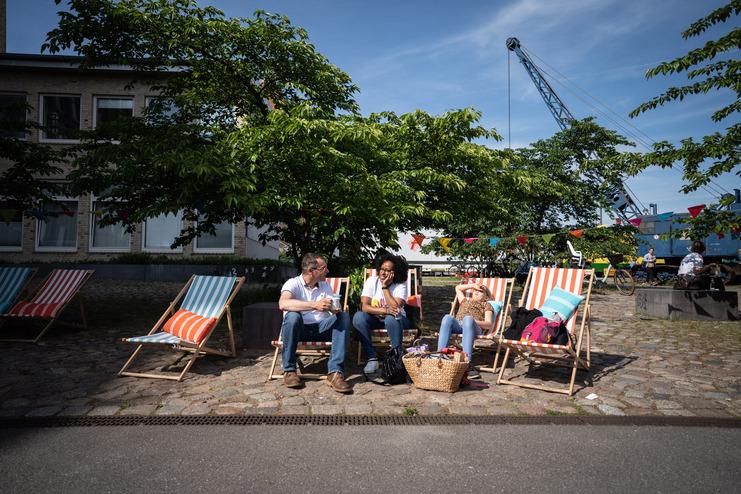 Tag der Nachbarn Zwei Personen sitzen in Liegestühlen unter einem Baum, während eine dritte Person in einem weiteren Liegestuhl entspannt.