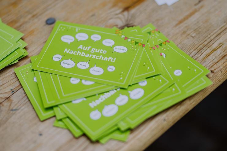 Tag der Nachbarn Stapels von grünen Karten mit dem Text „Auf gute Nachbarschaft!“ liegen auf einem Holztisch.